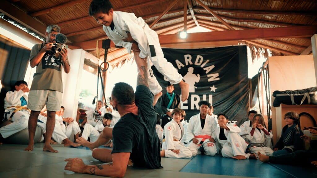 Fair Fight foundation group in gi holding up kid in gi above head while being photographed on the mat.
